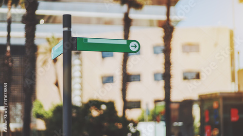 Narrow green waymark mock up with arrow inside of circle on street of summer city with blurred urban background with palms behind, sunny day, Barcelona, Spain photo