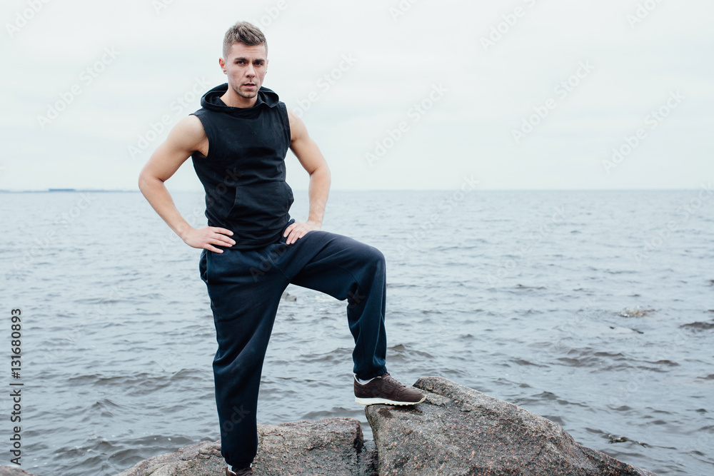 Strong yang fitness man poses on beach near sea and rocks.