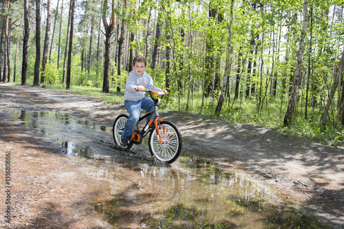 In the summer in the woods a little boy rides through a puddle o © tsomka
