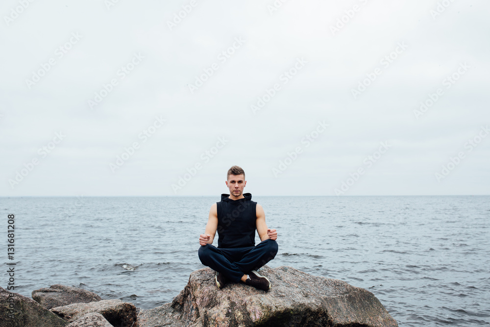 Strong fitness yoga man in lotus pose on the rock beach near the ocean. Harmonic concept.