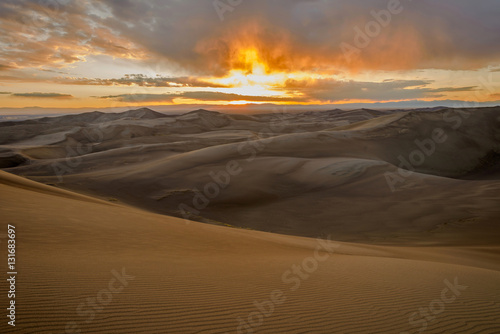 Sunset at Great Sand Dunes - Spring storm clouds passing over Great Sand Dunes as the sun sets at horizon. Great Sand Dunes National Park   Preserve  Colorado  USA.