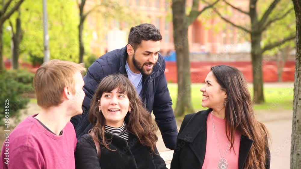 Group of friends having fun at park in Berlin. Mixed race group with caucasian, middle eastern and nordic persons, sitting on a bench and talking. Happiness and friendship concepts. Group of friends having fun at park in Berlin. Mixed race group with caucasian, middle eastern and nordic persons, sitting on a bench and talking. Happiness and friendship concepts.