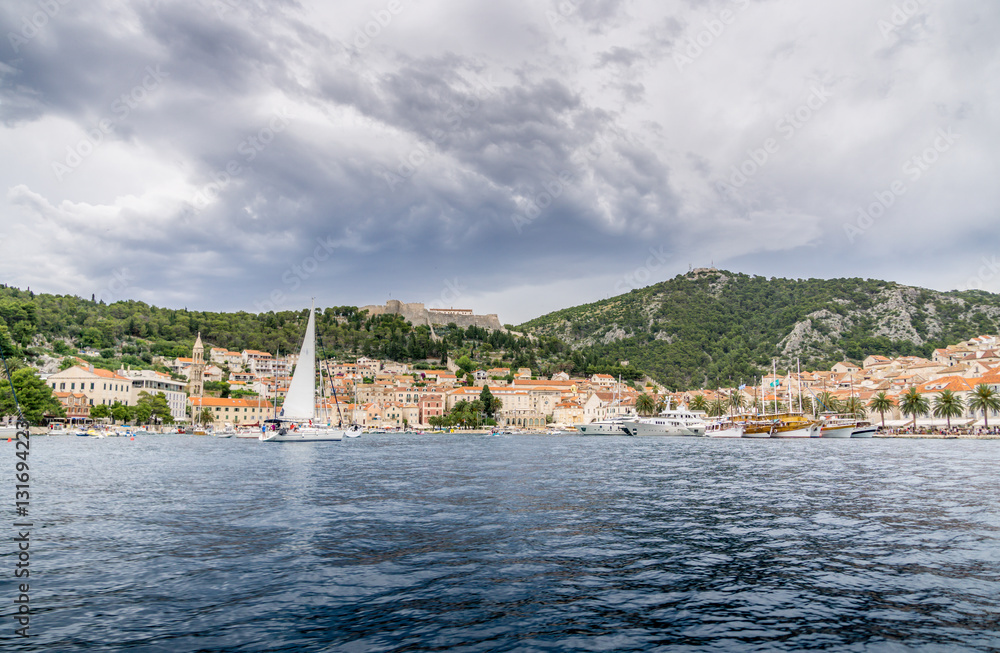 A boat sails into harbor in the old town of Hvar as a summer storm gathers over the ancient mountains behind the town.