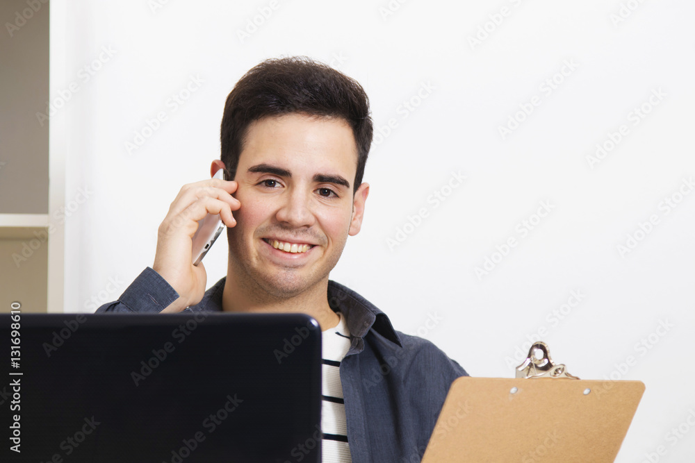 man smiling looking at camera with the phone mobile in front of the computer with them documents man smiling looking at camera with the phone mobile in front of the computer with them documents