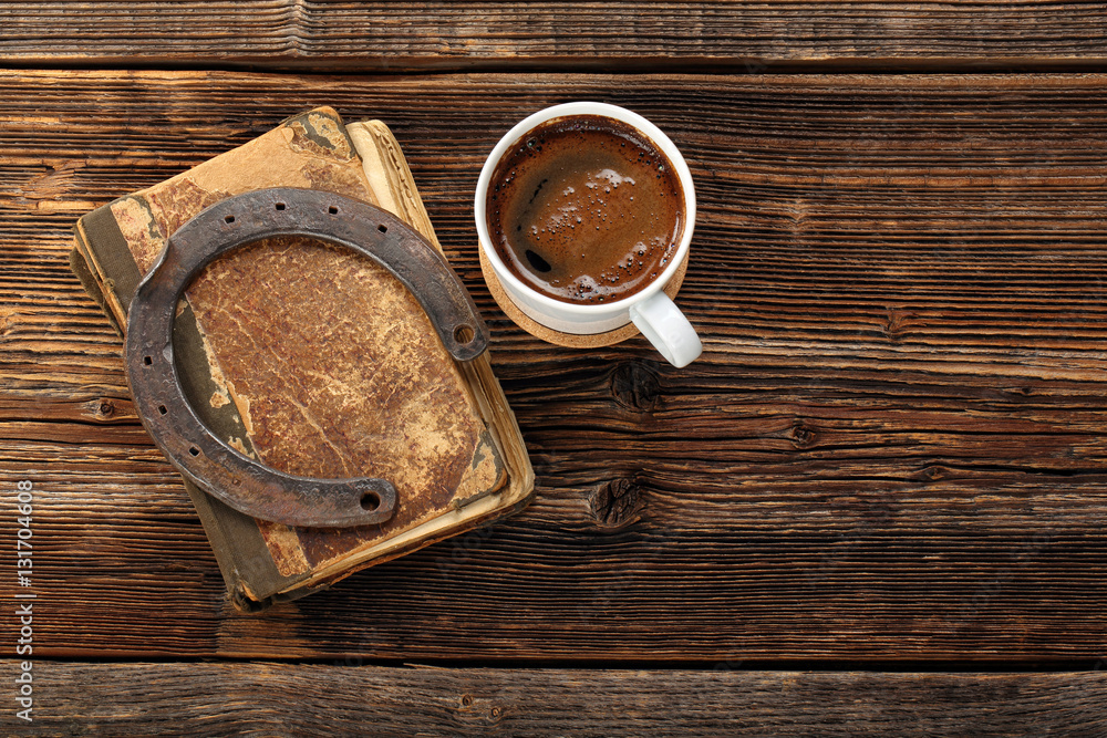 Naklejka premium Old book, rusty horseshoe and cup of coffee on wooden background