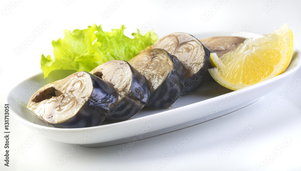 Pieces of mackerel and lemon on a white plate on a white background