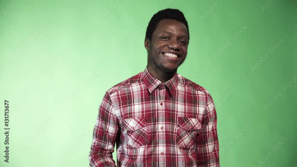 Young funny black man in plaid shirt smiling and giving thumbs-up on green chromakey background. 4K shot