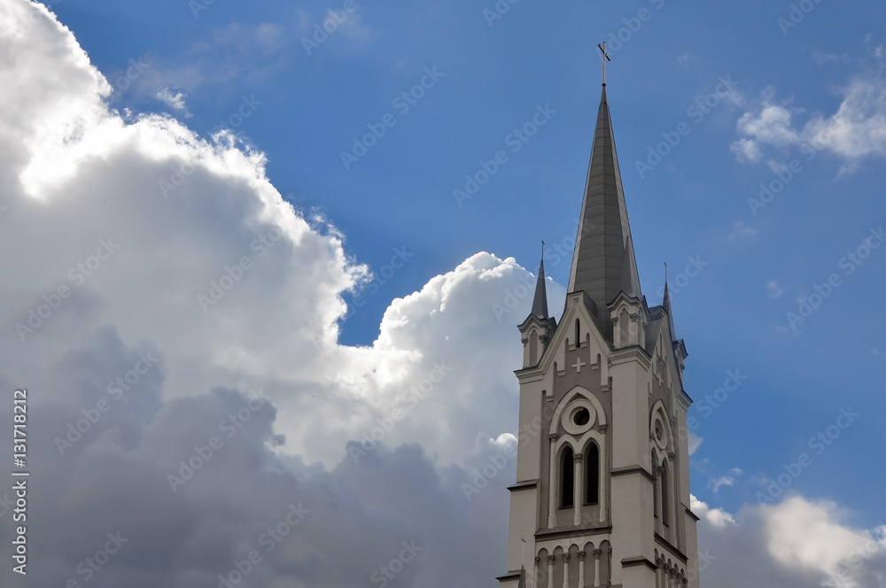 Old Gothic church tower spire on a background of white cumulus clouds and blue sky. Grodno, Belarus.