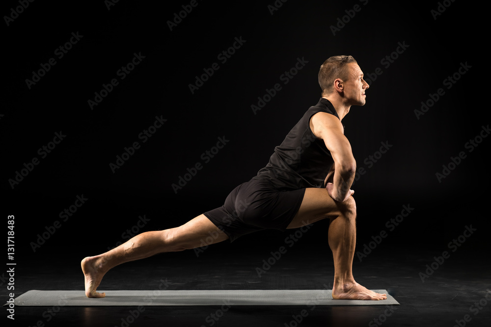 Man standing in yoga position in black sportwear on grey mat Man standing in yoga position in black sportwear on grey mat
