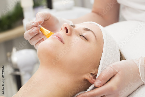 Beautiful young woman lying with closed eyes and cosmetologist applying facial mask