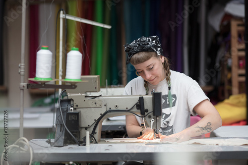 Young tattooed seamstress sewing in a factory environment