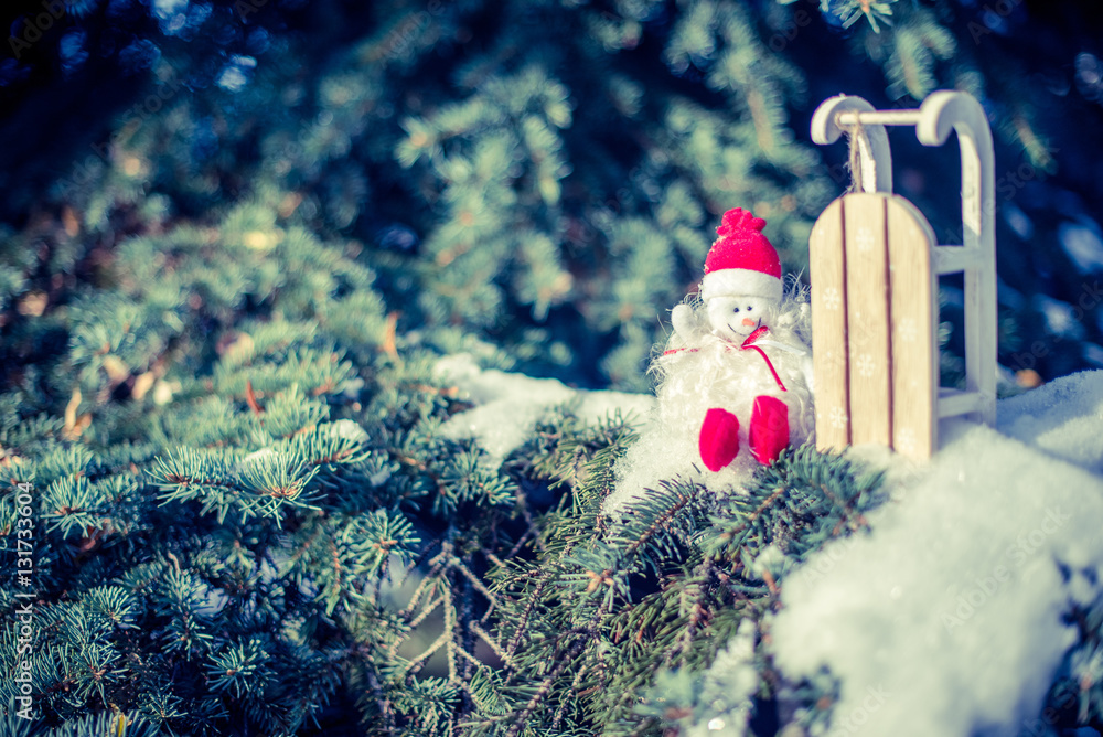 Obraz premium Snowman sitting near sled in the branches of fir