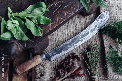 Big vintage kitchen knife surrounded by cooking ingredients - pepper, bok choy, thymus and parsley