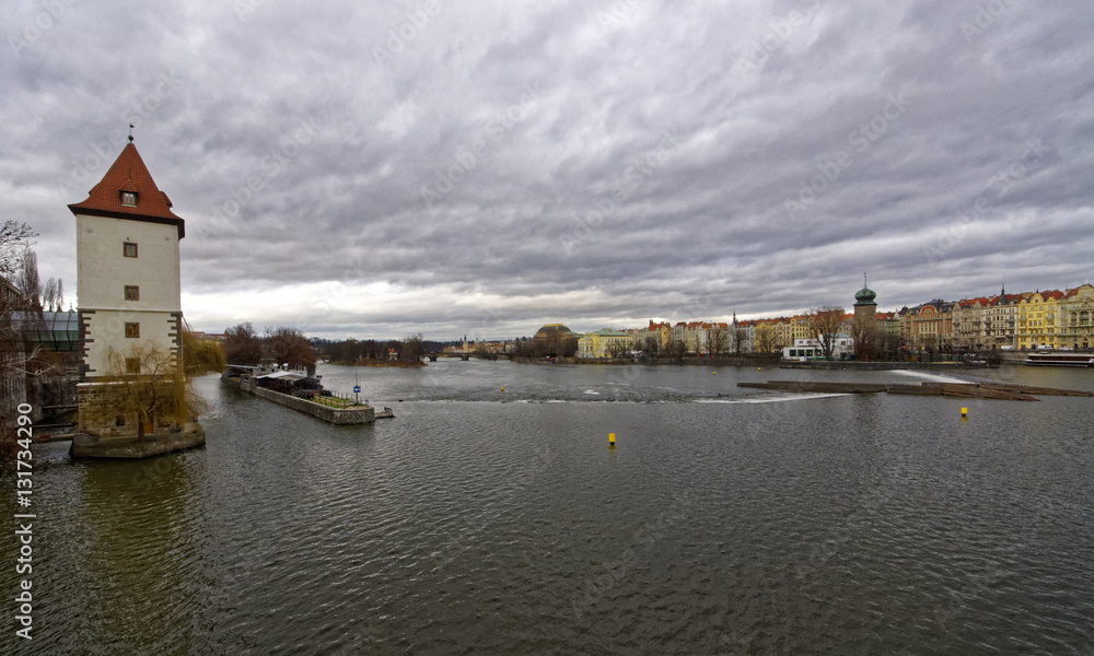 A beautiful photograph of the Vltava river with greenery lined on one bank and the city on the other