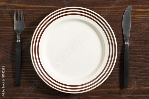 Empty plate with brown stripes and cutlery on brown wooden table  top view