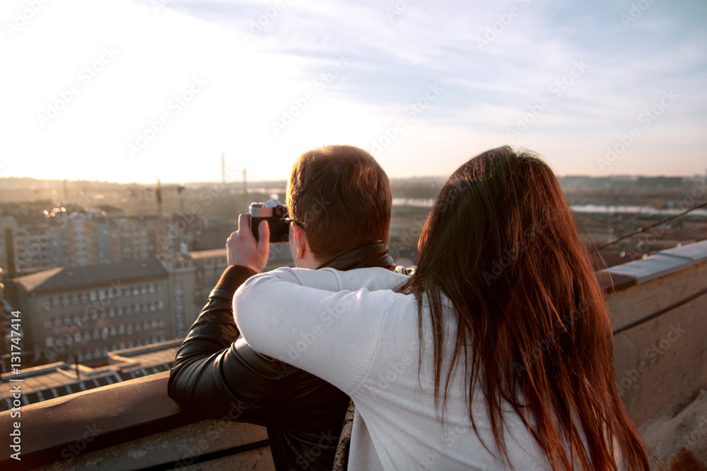 Couple taking pictures of the sunset on rooftop of the city