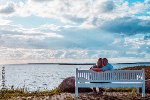 Loving couple sitting on the bench near the sea during the sunse