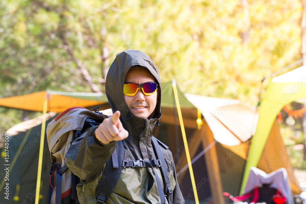 A hiking man dress up ready to go outdoor in front of tent at the
