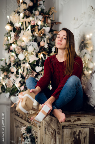 Woman with a Christmas Gift sitting on acncient commode decorated for xmas. Fir tree at background photo