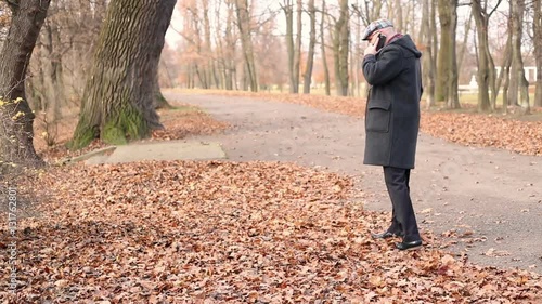 Grown man talking on cellphone, walking in the autumnal park
 photo