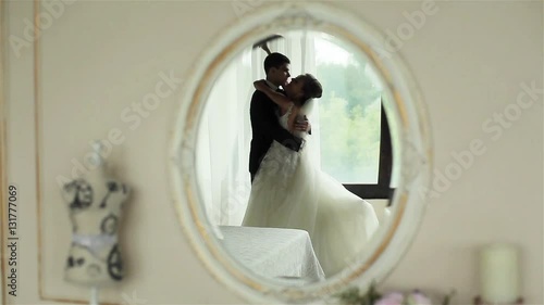 Happy newly wedded couple bride and groom embrace and kiss feeling happy reflected in mirror on wall of first night room interior. Happiness wedding honey moon marriage memories concept