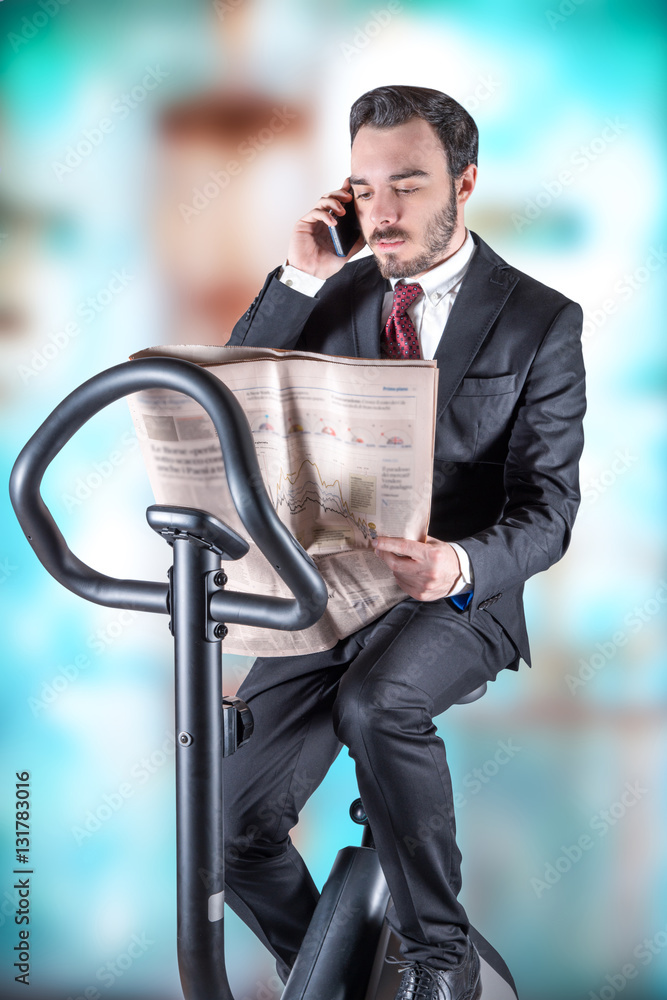 Stockfoto giovane che legge e parla al telefono sopra cyclette | Adobe Stock