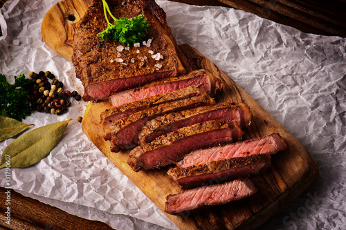 Fotografie Single roasted medium rare sliced flank beef piece with herbs over wooden bord