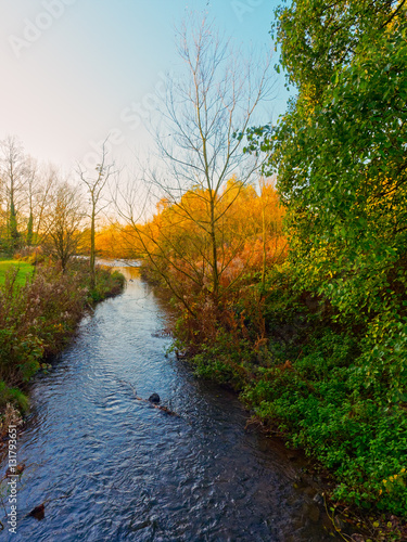 The River Leen flowing gently towards a lake on a bright autumn morning.