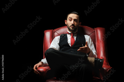 side view of an elegant young businessman smoking a cigarette on black studio background photo