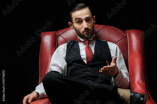 side view of an elegant young businessman smoking a cigarette on black studio background photo