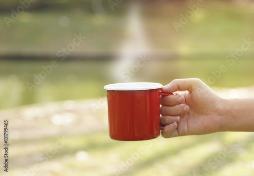 hand holding red coffee cup in blur green gardent background