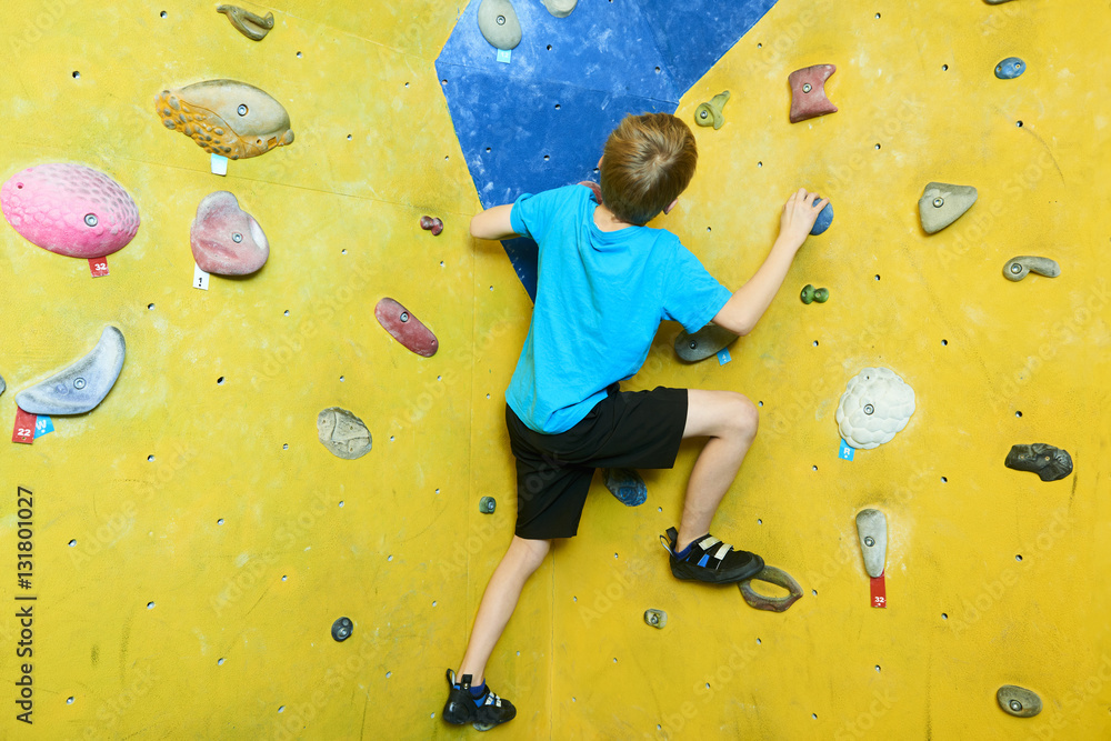 Fototapeta premium Free climber child young boy practicing on artificial boulders in gym, bouldering