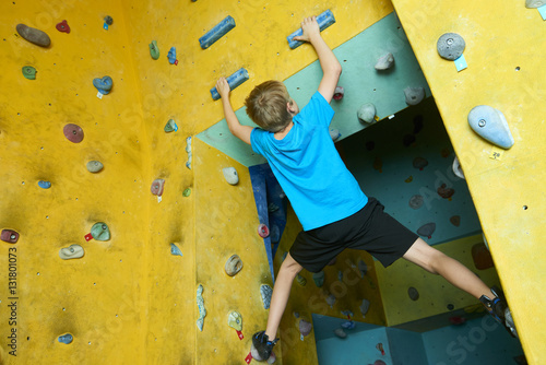 Free climber child young boy practicing on artificial boulders in gym, bouldering
