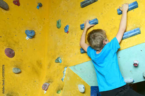 Free climber child young boy practicing on artificial boulders in gym, bouldering
