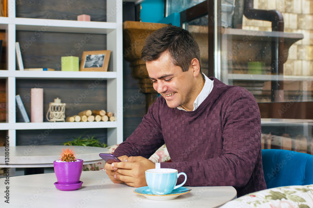 Young man holding a mobile phone and smiling. Read the posts and drinking coffee. Young man holding a mobile phone and smiling. Read the posts and drinking coffee.