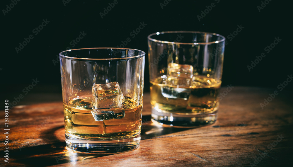 Glasses whiskey and ice cubes on wooden counter