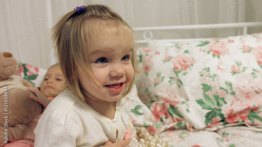 Adorable little girl sitting on a bed with her sister Adorable little girl sitting on a bed with her sister