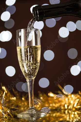Bottiglia che versa in bicchiere flute vino spumante, con luci di sfondo e decorazioni festive photo
