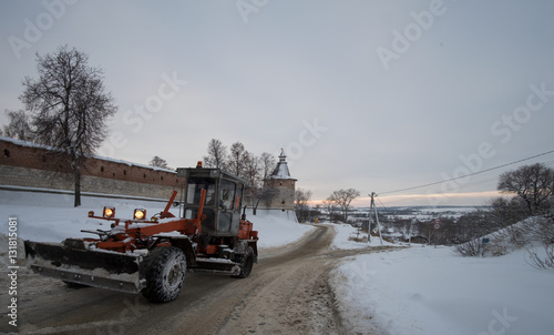 Снегоуборочный трактор с широкой лопатой едет по дороге зимним вечером  © androsov858