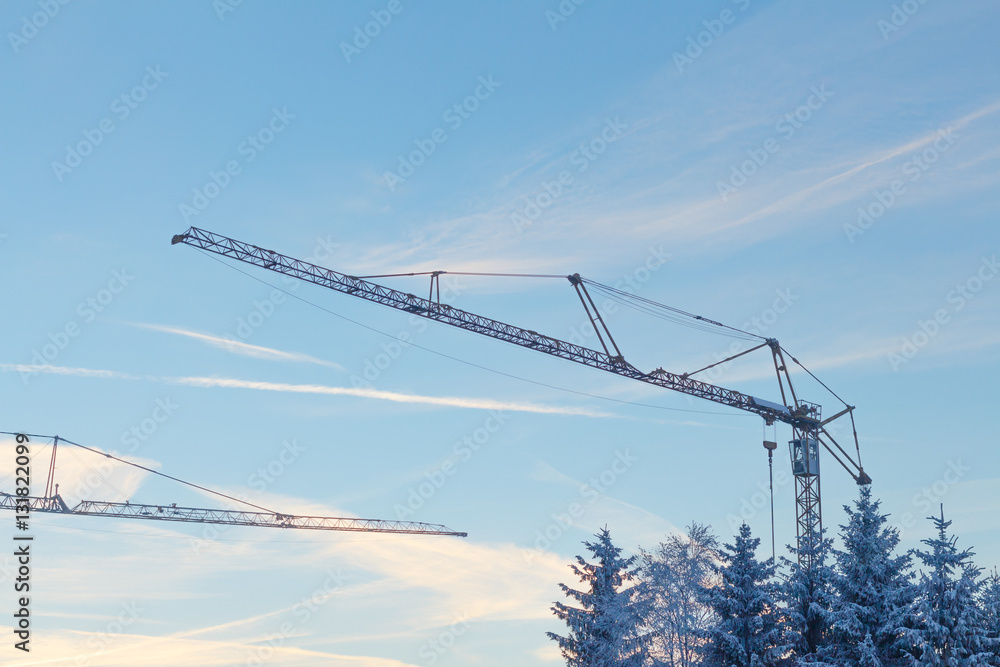 Two cranes on construction side in winter with blue sky