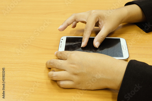 Office lady hand in a black suit pressing a smart phone screen on a wood desk background