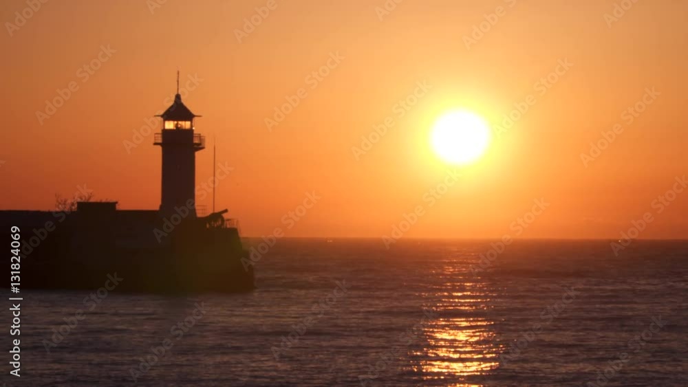Lighthouse illuminated by the rising sun. The sun is reflected in water Lighthouse illuminated by the rising sun. The sun is reflected in water