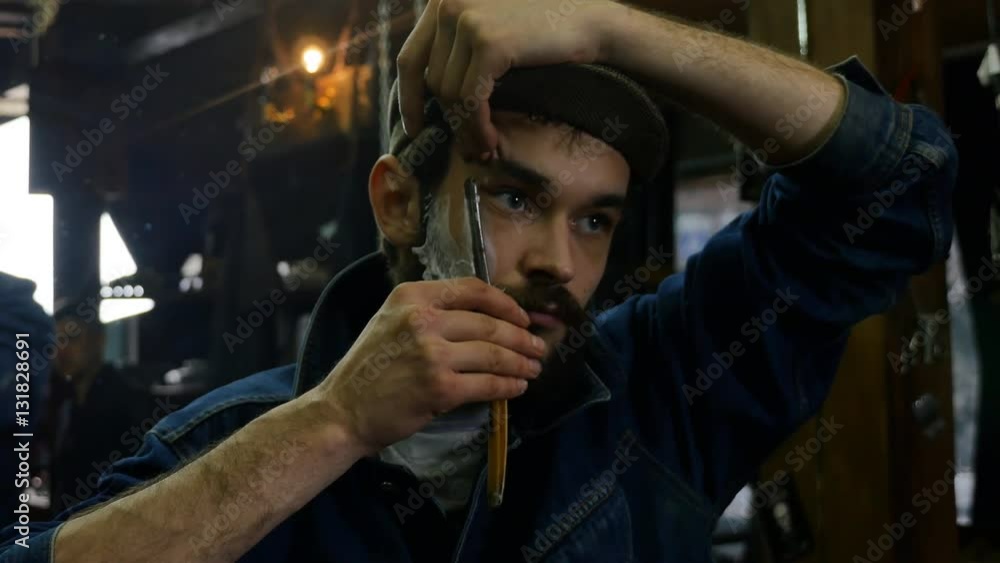 Handsome man shaving in barbershop with foam and manual dangerous razer. Young barber shaves himself Handsome man shaving in barbershop with foam and manual dangerous razer. Young barber shaves himself