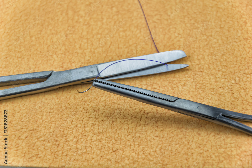 Obraz premium Real sterilized needle holder with purple suture and scissors in front of skin imitating textured background.