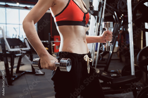 Torso of a young fitness woman with lifting dumbbells at gym