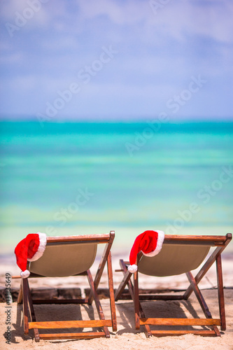 Sun loungers with Santa hat at tropical beach with white sand and turquoise water