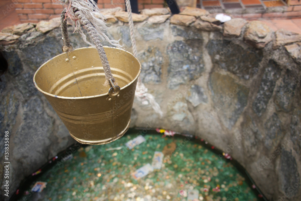 A golden bucket hanging above a little fountain made of stone.