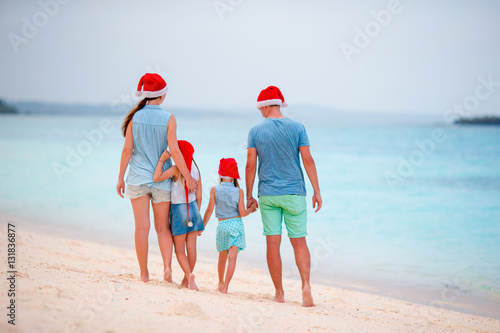 Happy beautiful family in red Santa hats on tropical beach celebrating Christmas