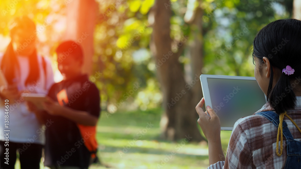 Asian students playing a tablet with sun shining in the park Asian students playing a tablet with sun shining in the park