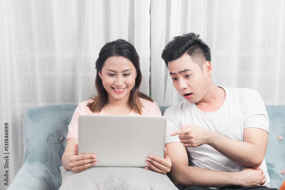 Young couple surfing on internet with laptop. Modern white apartment in background